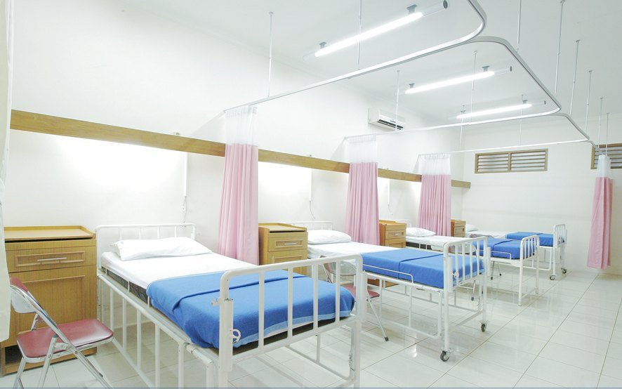 Bright, clean hospital ward featuring multiple beds with blue bedding