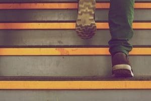 A person ascends a set of stairs with bright orange and gray contrasting steps, emphasizing motion and the urban environment.