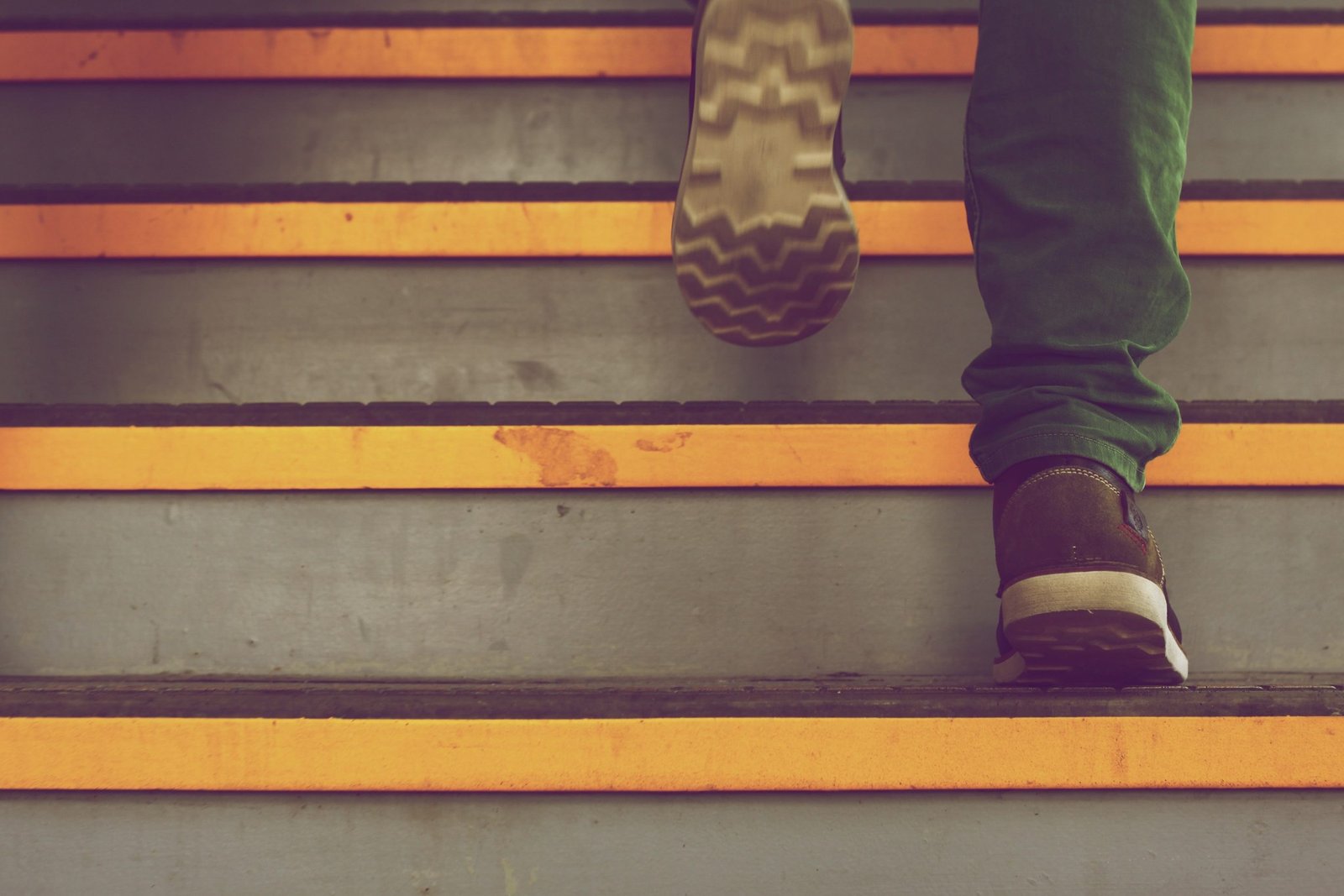 A person ascends a set of stairs with bright orange and gray contrasting steps, emphasizing motion and the urban environment.