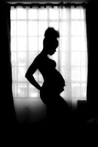 Silhouette of a pregnant woman posing gracefully against a window's diffused light, illustrating the beauty of maternity and motherhood.