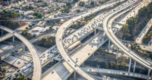 Aerial view of a busy highway interchange surrounded by urban development, showcasing multiple lanes of traffic and roadways intersecting.
