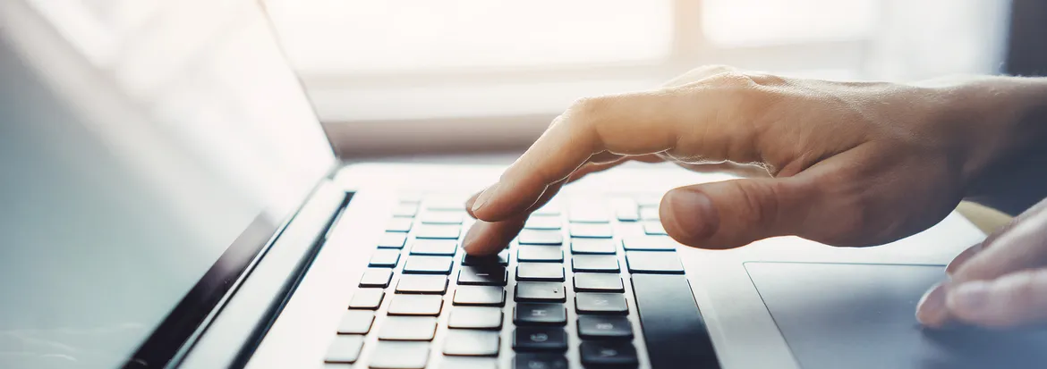 Fingers poised above a laptop keyboard, capturing the act of typing. The image conveys focus and productivity in a modern work setting.