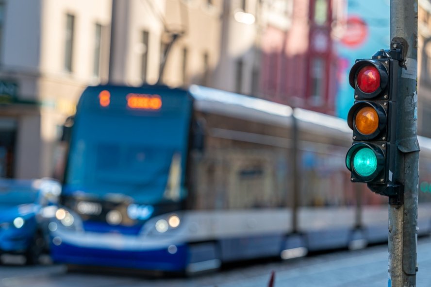 Traffic signal displaying green light, with a blurred public transport bus approaching in an urban setting. Highlights transportation flow.