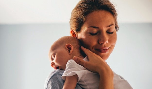 Mother gently cradles her sleeping infant, showcasing a tender bond in a serene setting. The image emphasizes love and nurturing.