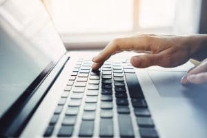 Close-up of female hands typing on the laptop keyboard, woman's hands using laptop in interior, filtered sunlight image