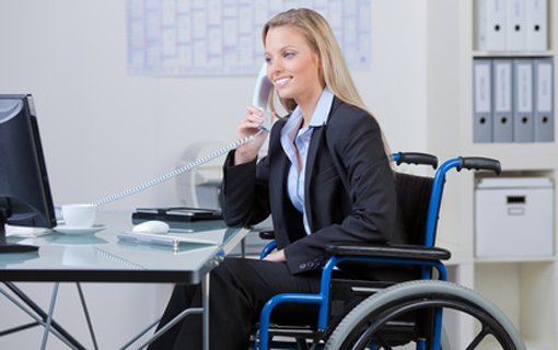 A businesswoman in a wheelchair talks on the phone while working at her desk, demonstrating professionalism and accessibility in the workplace.
