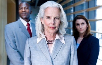 Older woman in business suit with 2 coworkers standing behind her at an office window
