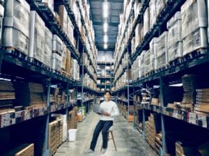 young man working in a warehouse sitting on a stool as the only seat he could find