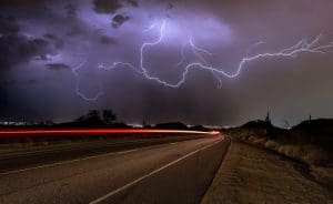 lightning illuminates a stormy night sky above a winding road