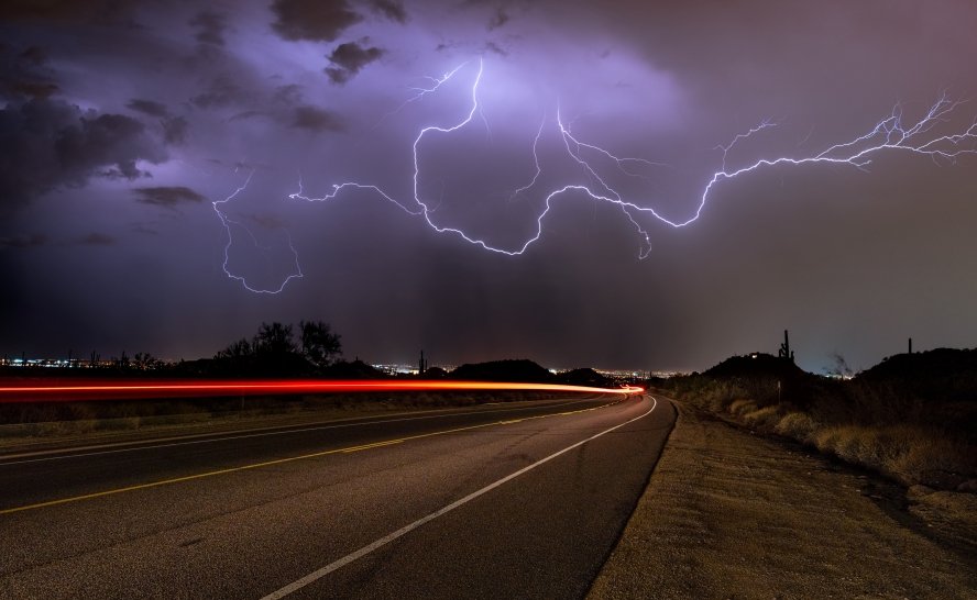 lightning illuminates a stormy night sky above a winding road